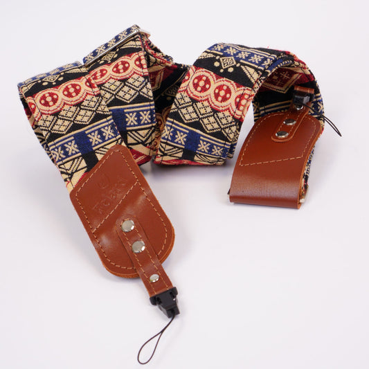 A patterned camera strap with brown leather ends and silver metal hardware, photographed on a plain white background.