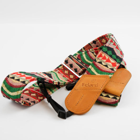 A patterned camera strap with a Southwestern geometric design in red, green, beige, and black, featuring a tan leather end cap embossed with the brand 'Felard'.