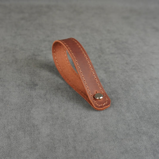 dark cognac matte leather strap headstock adapter with a single silver metal rivet, photographed on a textured gray background.