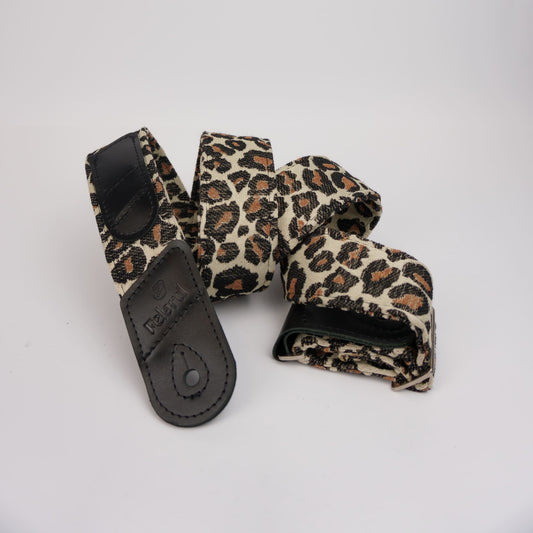 A leopard print guitar strap with black leather accents, coiled on a plain white background.