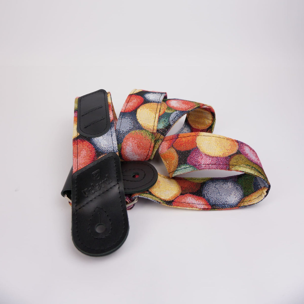 A camera strap featuring a colorful print with red, yellow, orange, and green motifs on a white background, finished with black leather hardware.