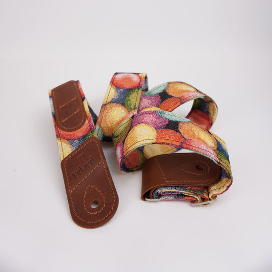 Guitar strap with a colorful fruit print and brown leather ends, shown on a plain white background.