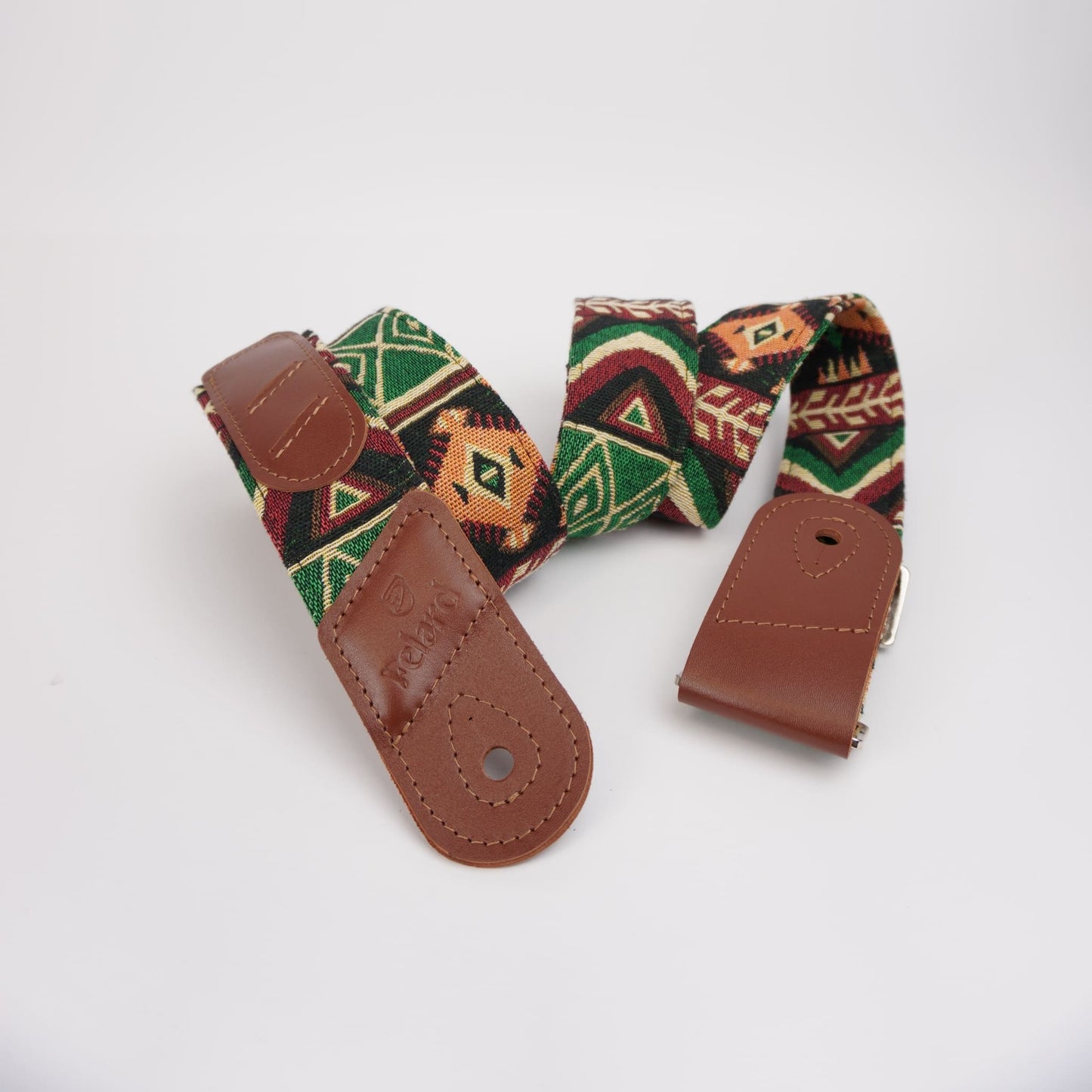 A guitar strap with a brown leather end pieces and a woven fabric body featuring a Southwestern geometric pattern in green, red, orange, and black, displayed on a clean white background.