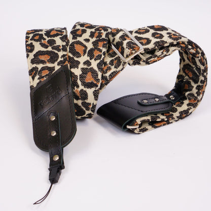 A leopard print canvas camera strap with black leather ends and silver-tone metal hardware, displayed on a clean white background.