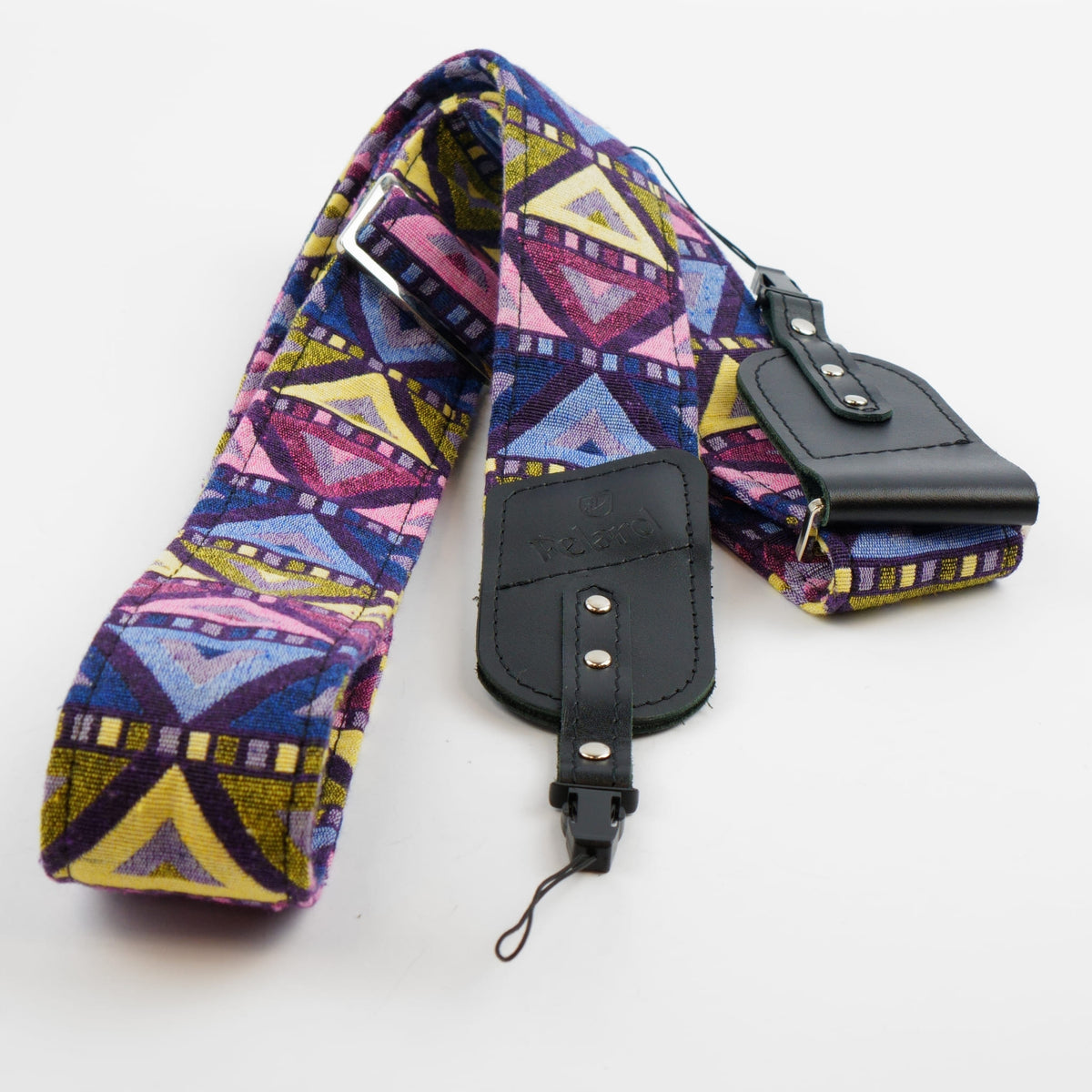 A fabric camera strap with a colorful geometric pattern in purple, pink, yellow, and blue, featuring black leather hardware and a matching pouch on a white background.