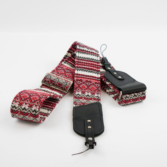 A patterned camera strap with red, black, and white geometric designs, featuring black leather quick-release buckles and a matching black leather pouch on a white background.