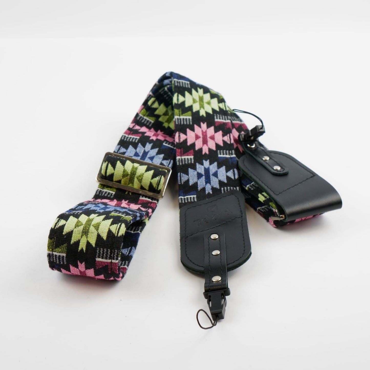 A wide fabric camera strap with a colorful geometric pattern in pink, green, blue, and black, featuring a black leather buckle and a matching black leather pouch on a white background.
