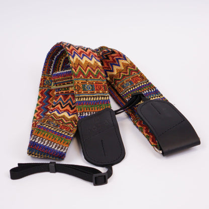 A woven camera strap with a vibrant multicolor geometric pattern, featuring black leather ends and a black adjustable wristlet strap, displayed on a clean white background.