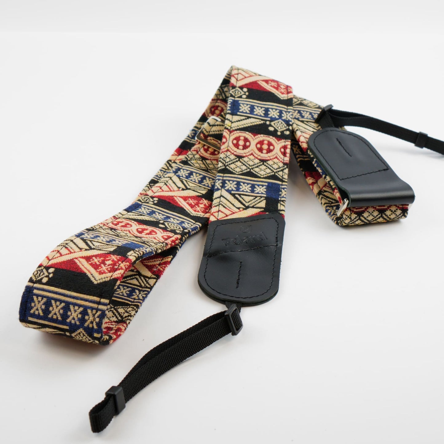A camera strap with a colorful geometric pattern in red, blue, beige, and black, featuring black padded leather-like loops and a black adjustable strap.