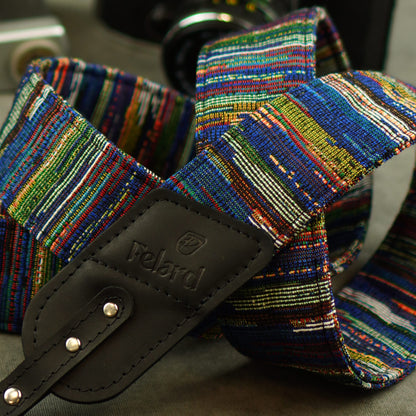 A close-up of a multicolored woven camera strap with a black leather and the brand name Felard embossed on it.