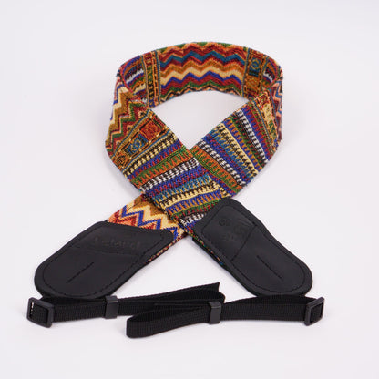 A woven camera strap with a vibrant multicolor geometric pattern, featuring black leather ends displayed on a clean white background.