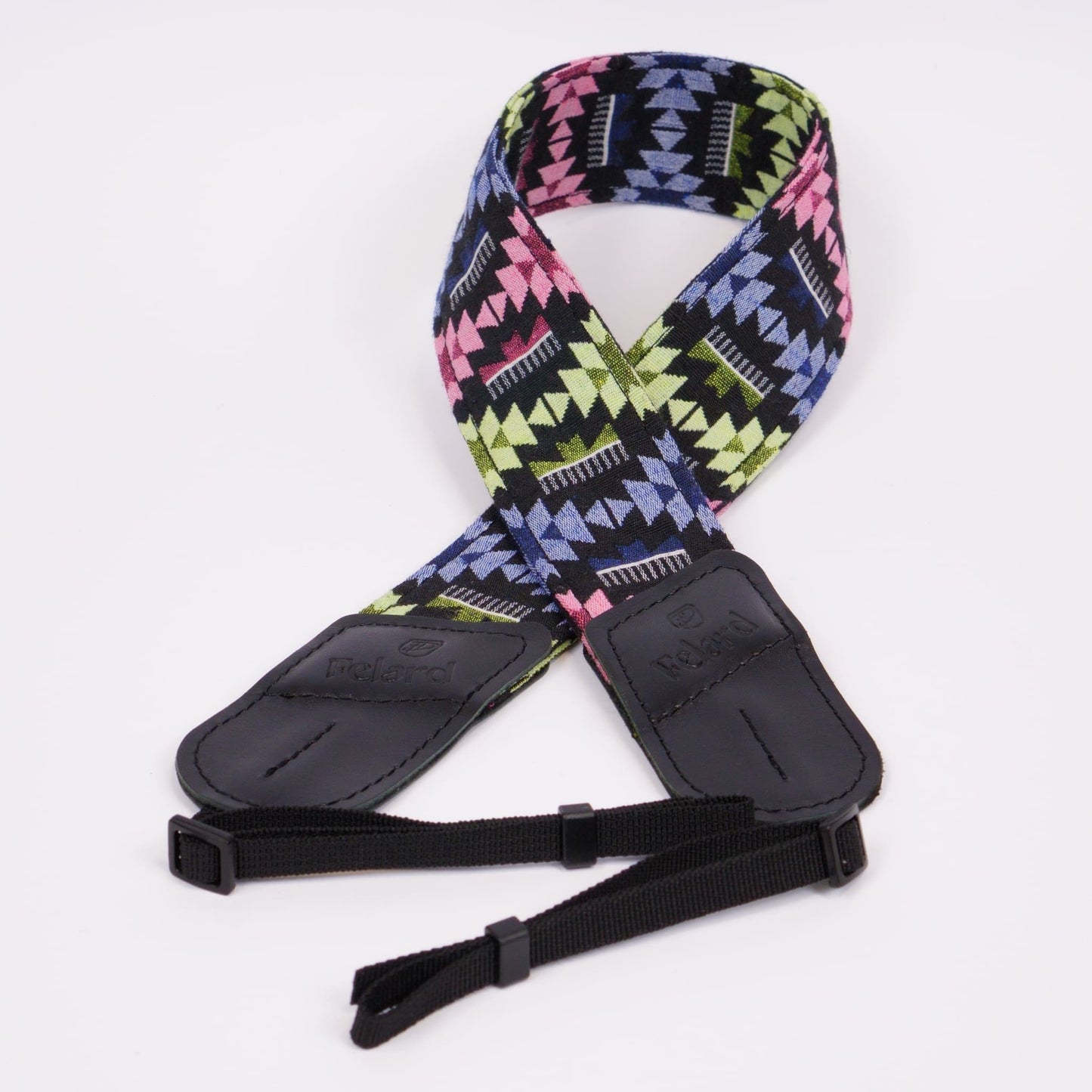 A camera strap featuring a vibrant geometric pattern in pink, lime green, blue, and black, with black leather ends and adjustable black webbing.