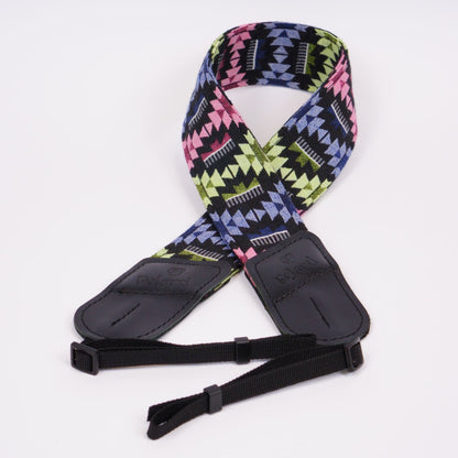 A camera strap featuring a vibrant geometric pattern in pink, lime green, blue, and black, with black leather ends and adjustable black webbing.