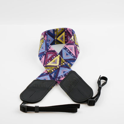 A camera strap featuring a vibrant geometric tribal pattern in pink, purple, blue, and yellow, with black leather end caps and a black adjustable wrist strap, shown on a light gray background.