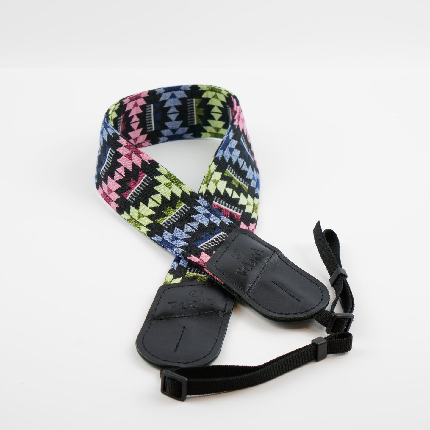 A camera strap featuring a vibrant geometric Southwestern pattern in pink, lime green, blue, and black, with black padded leather ends and an adjustable black webbing strap.