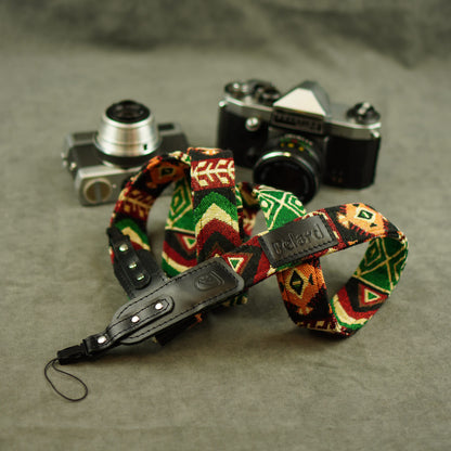 Patterned camera strap with a black leather wristlet and a visible 'Felard' tab, arranged in front of two vintage cameras on a textured gray surface.