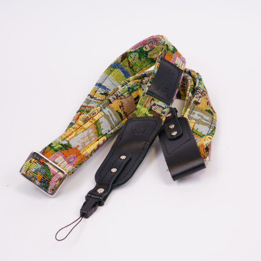 A camera strap featuring a colorful landscape patterned fabric and black leather accents, displayed on a clean white background.