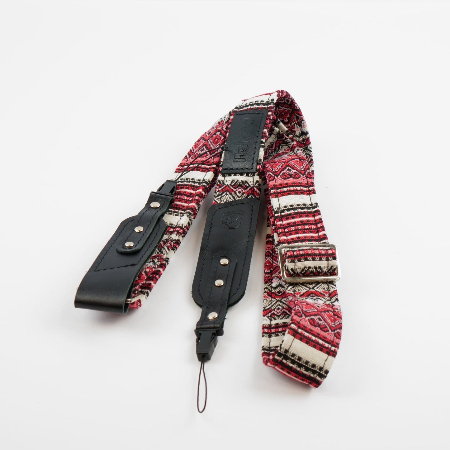 A camera strap featuring a red, black, and white geometric patterned fabric body with black leather accents and silver-tone metal rivets, displayed on a clean white background.