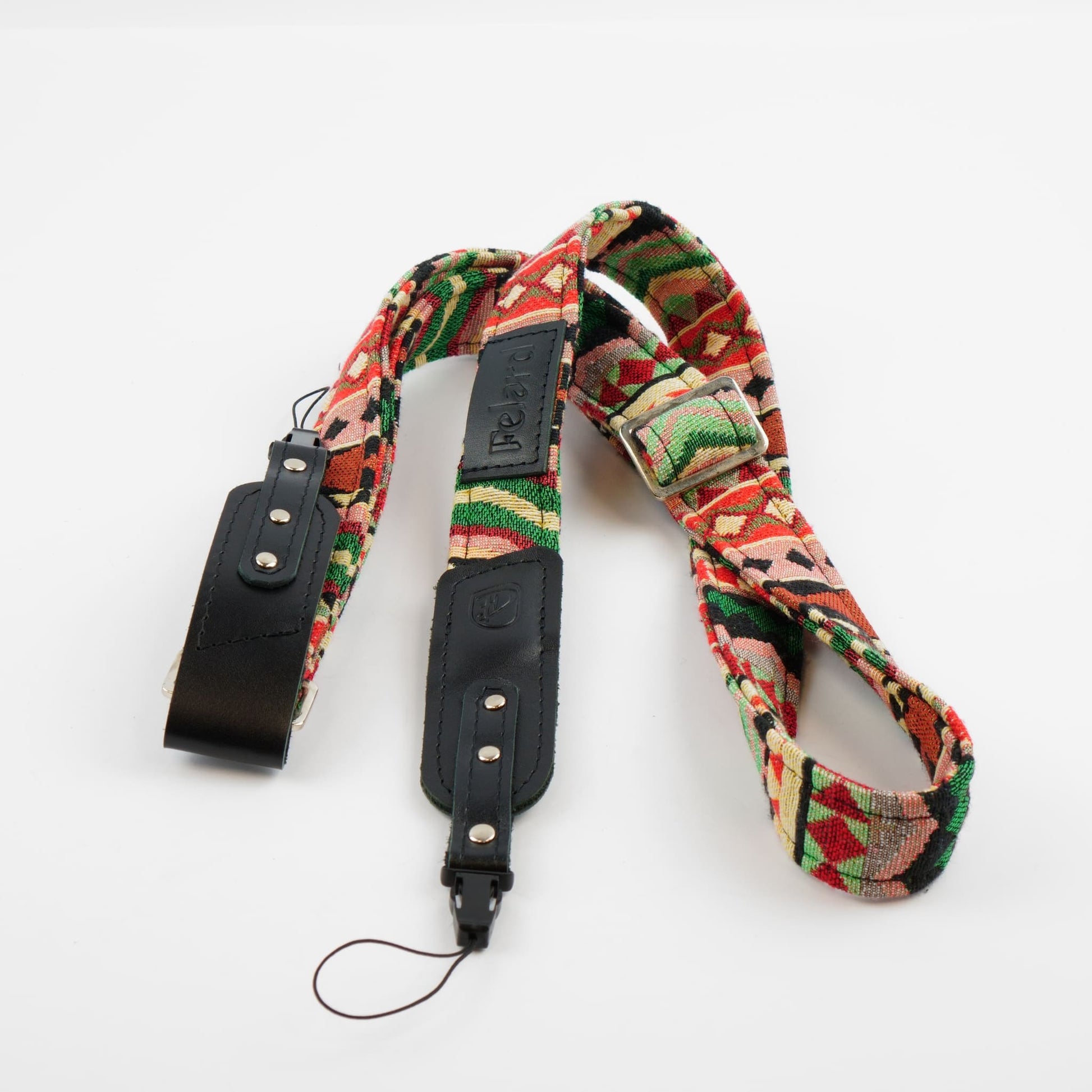 A camera strap featuring a colorful geometric patterned fabric with black leather sections and silver-tone metal hardware, displayed on a clean white background.