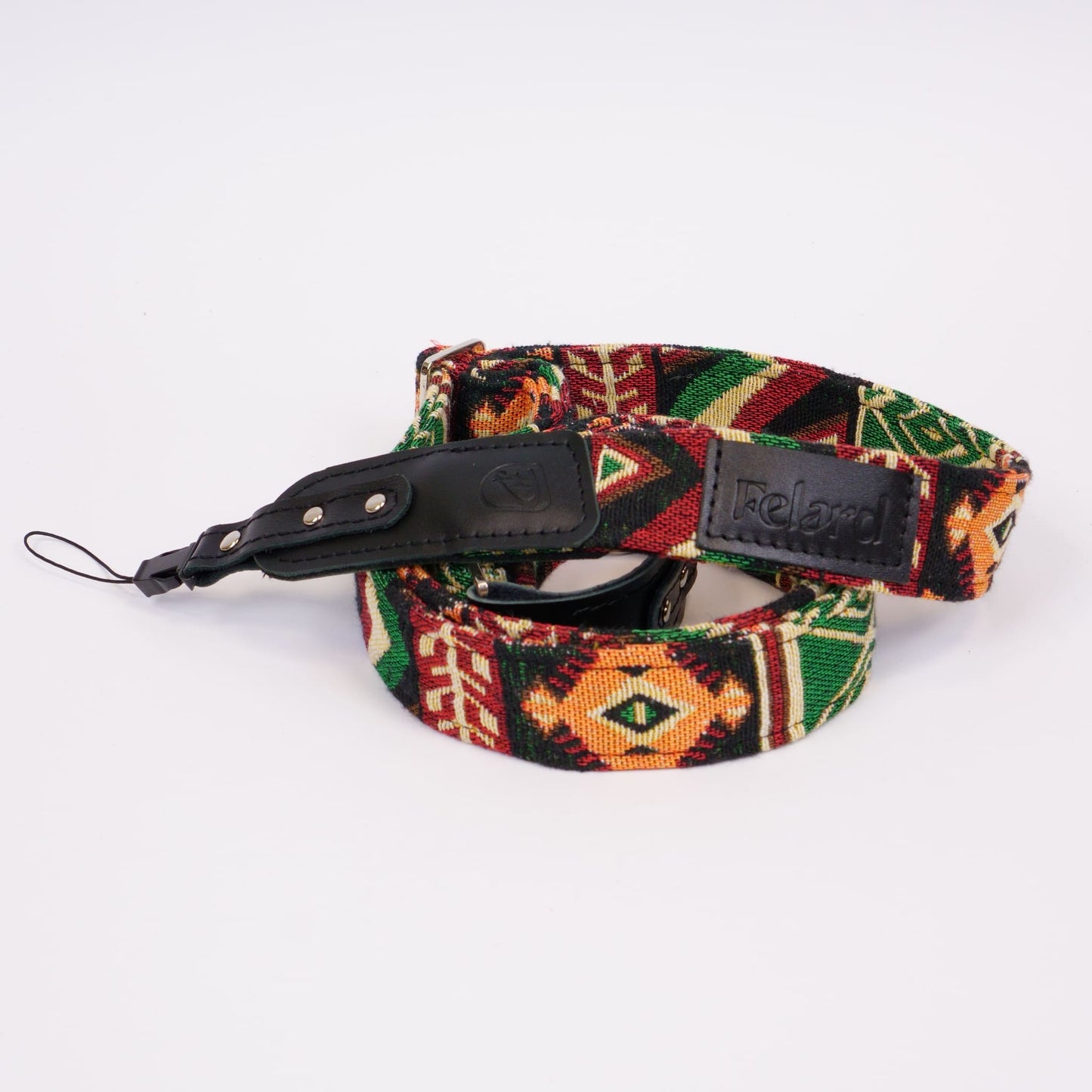 A woven camera strap with a Southwestern geometric pattern in red, green, black, and orange, featuring a black leather buckle and a black leather brand patch that reads 'Felard'.