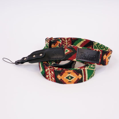 A woven camera strap with a Southwestern geometric pattern in red, green, black, and orange, featuring a black leather buckle and a black leather brand patch that reads 'Felard'.