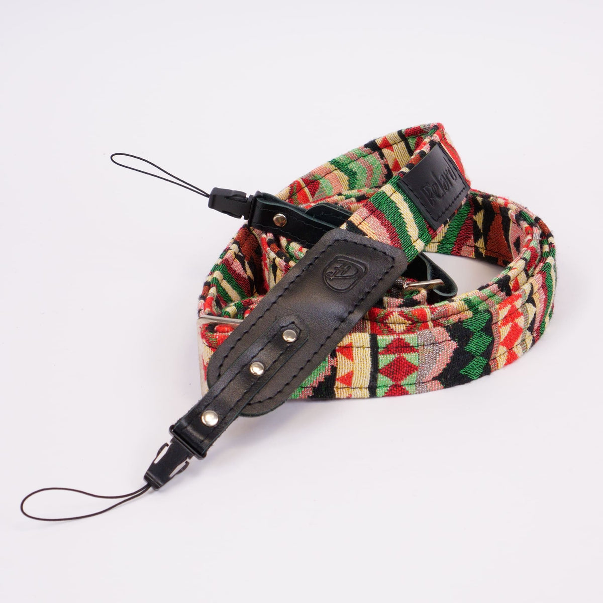 A woven camera strap with a vibrant geometric pattern in red, green, yellow, and black, featuring a black leather buckle and a matching leather keeper loop.