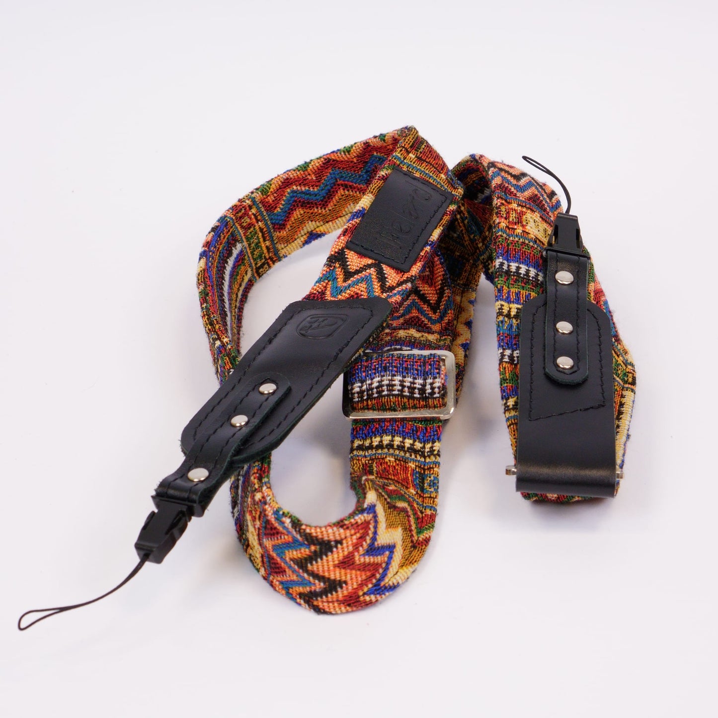 A multicolor patterned camera strap with black leather accents and silver metal hardware, photographed on a clean white background.
