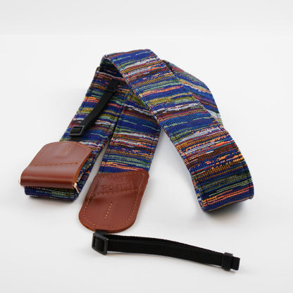 A multicolor woven camera strap with brown leather end caps and a black quick-release buckle strap, displayed on a clean white background.