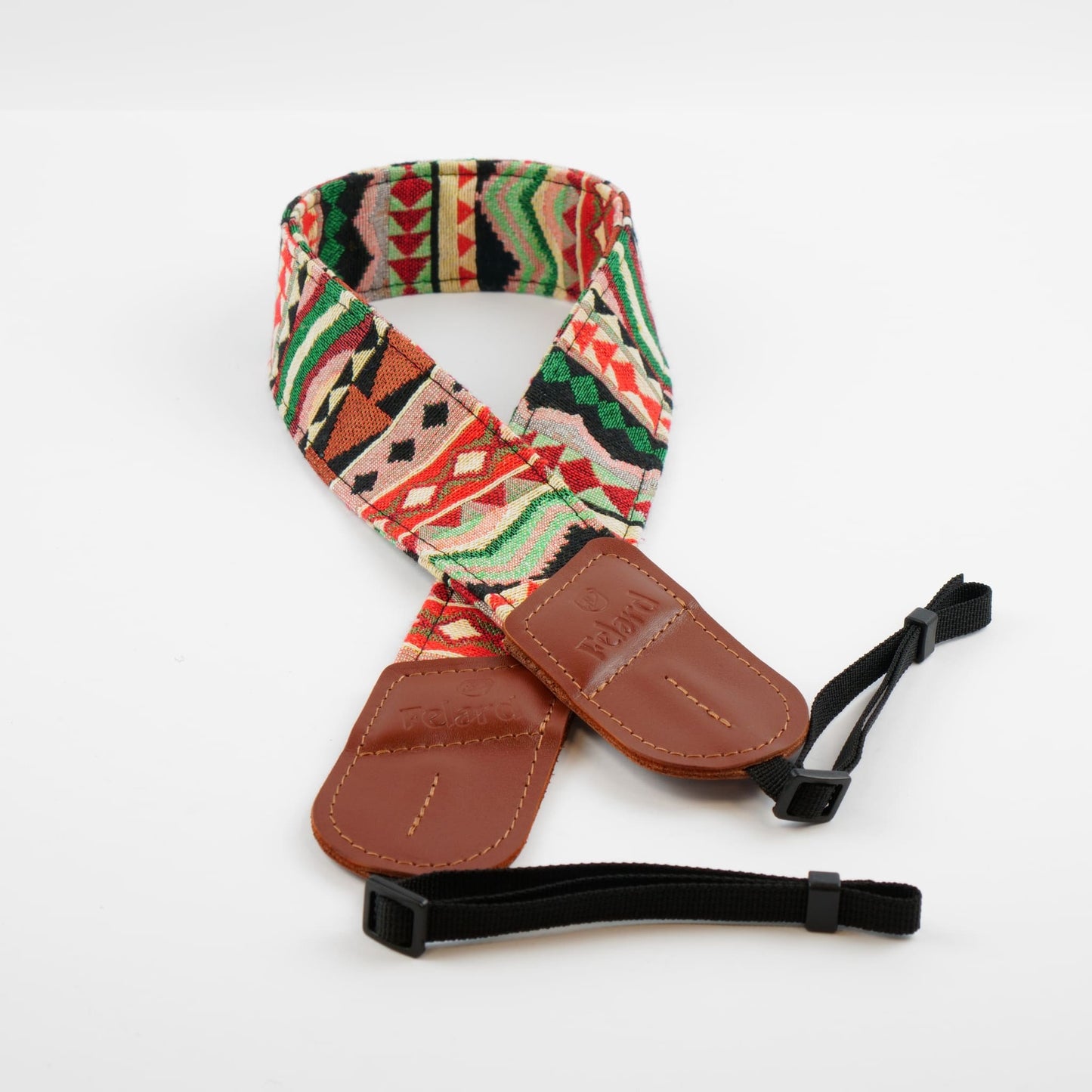 A camera strap featuring a colorful Southwestern geometric pattern in red, green, beige, and black, with brown leather end pieces and black adjustable nylon ties, displayed on a clean white background.