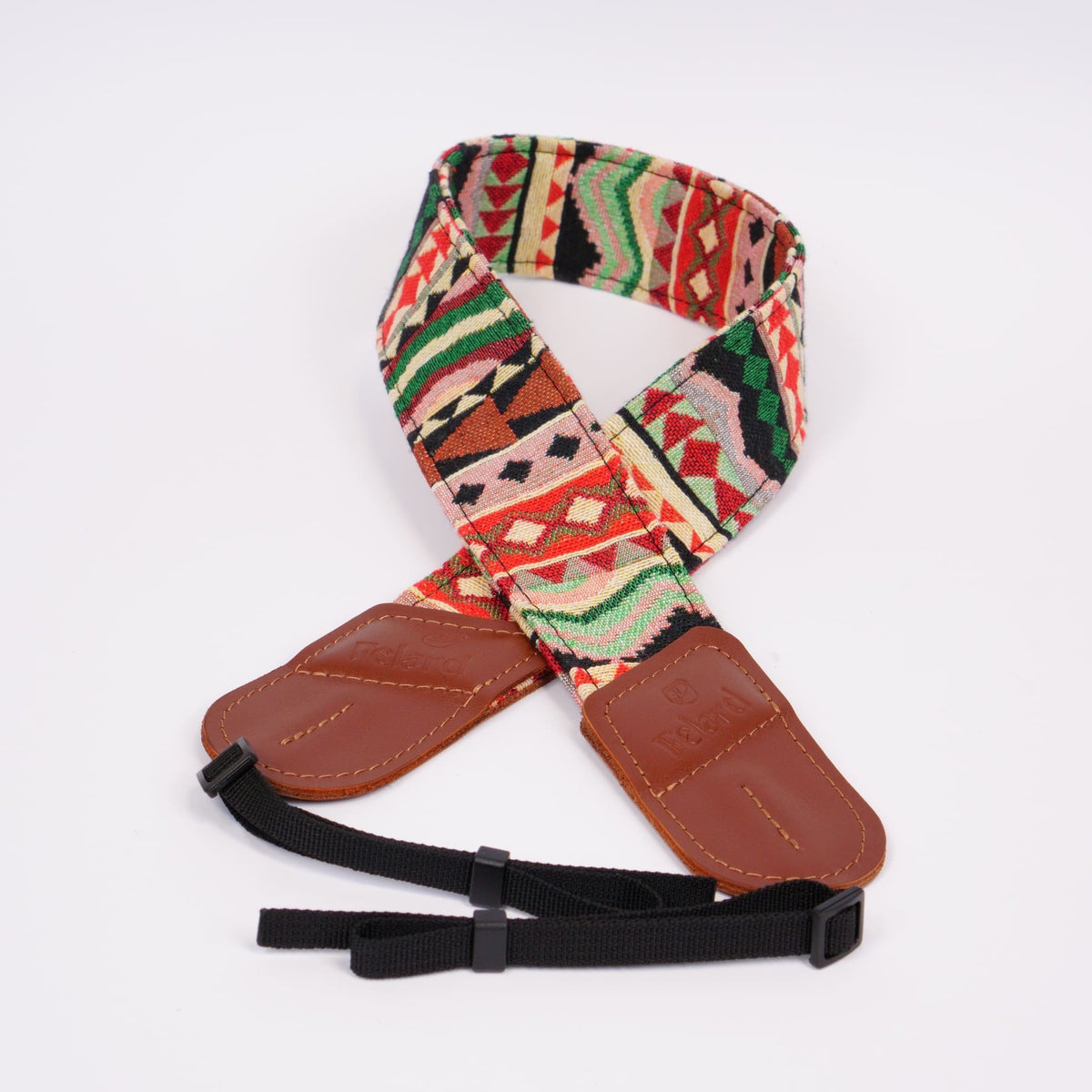 A camera strap featuring a colorful Southwestern geometric pattern in red, green, beige, and black, with brown leather ends and a black adjustable webbing strap.