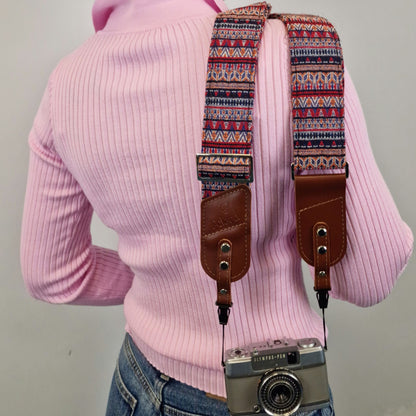 A person shown from the back while wearing a colorful geometric patterned camera strap with brown leather attachments. A vintage silver camera is hanging from the strap.