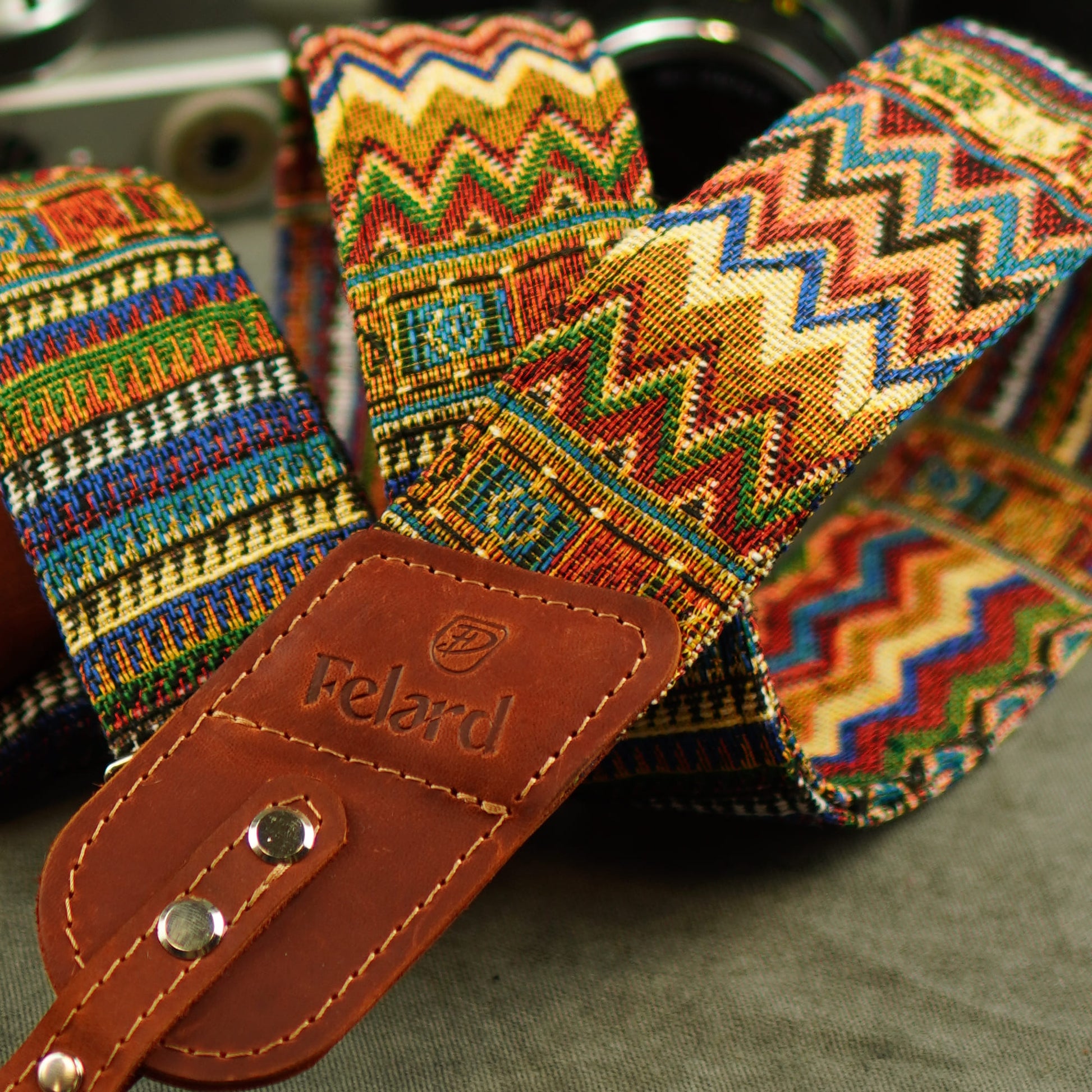 A close-up of a colorful woven camera strap with a brown leather Felard, featuring a multicolor zigzag pattern.