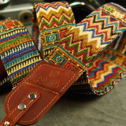 A close-up of a colorful woven camera strap with a brown leather Felard, featuring a multicolor zigzag pattern.