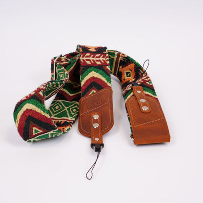 A camera strap featuring a colorful Southwestern geometric patterned fabric and brown leather accents, displayed on a clean white background.