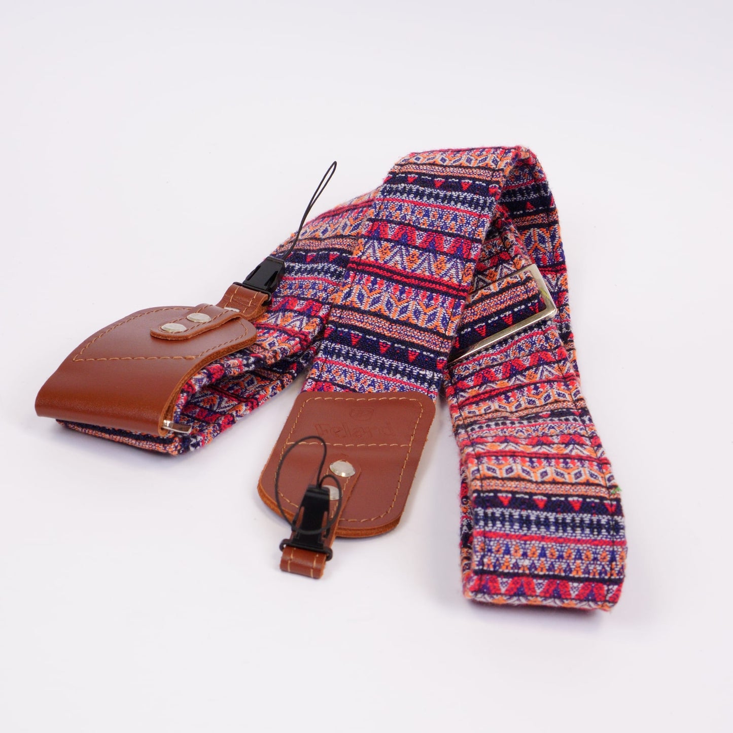 A woven camera strap with a colorful geometric pattern in red, blue, and beige, featuring brown leather ends and a metal buckle, displayed on a clean white background.