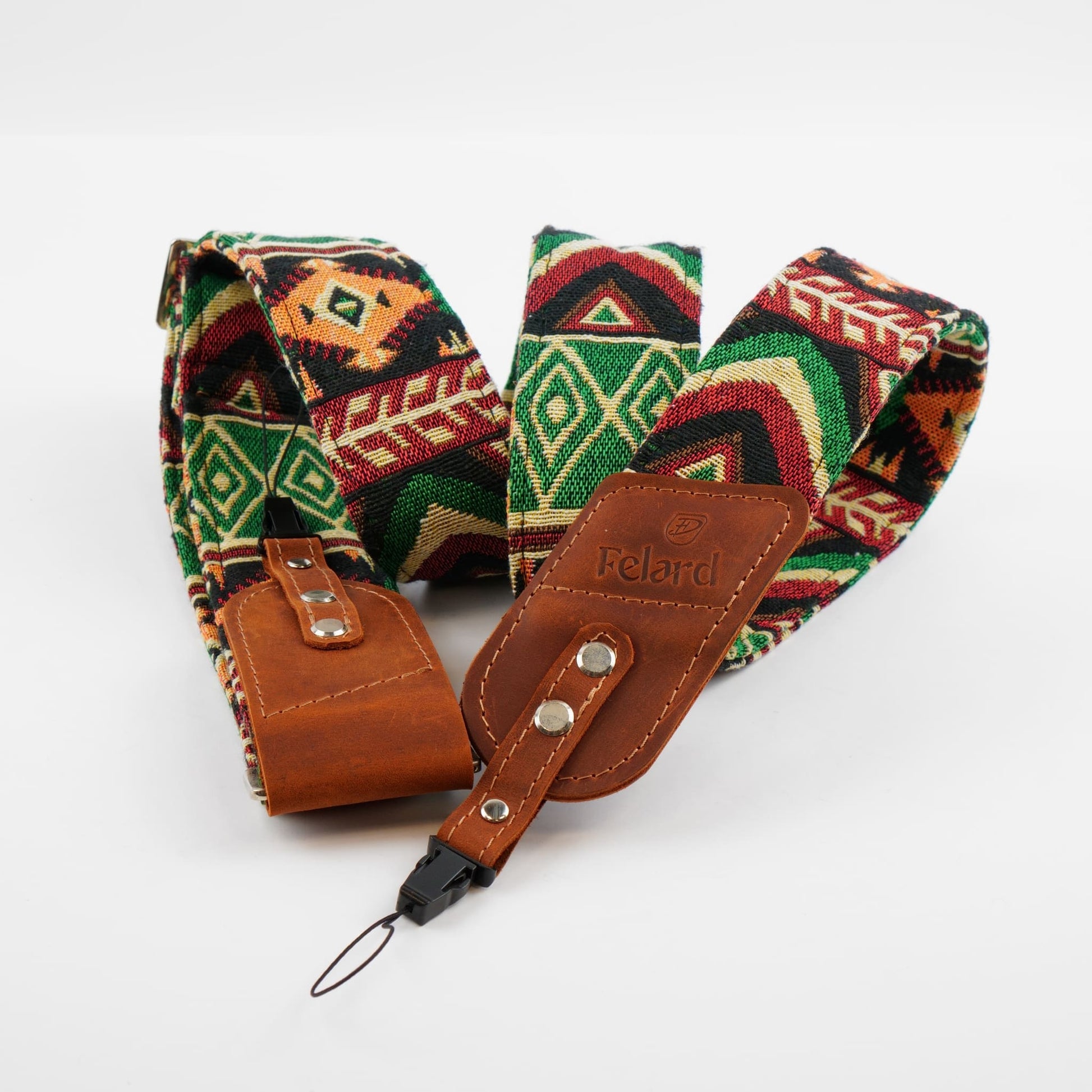 A patterned camera strap with a brown leather and a black carabiner clip, displayed on a clean white background. The fabric features a Southwestern geometric design in green, red, black, and beige.