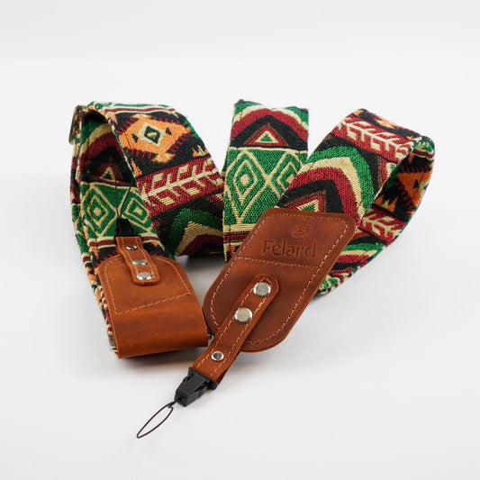 A patterned camera strap with a brown leather and a black carabiner clip, displayed on a clean white background. The fabric features a Southwestern geometric design in green, red, black, and beige.