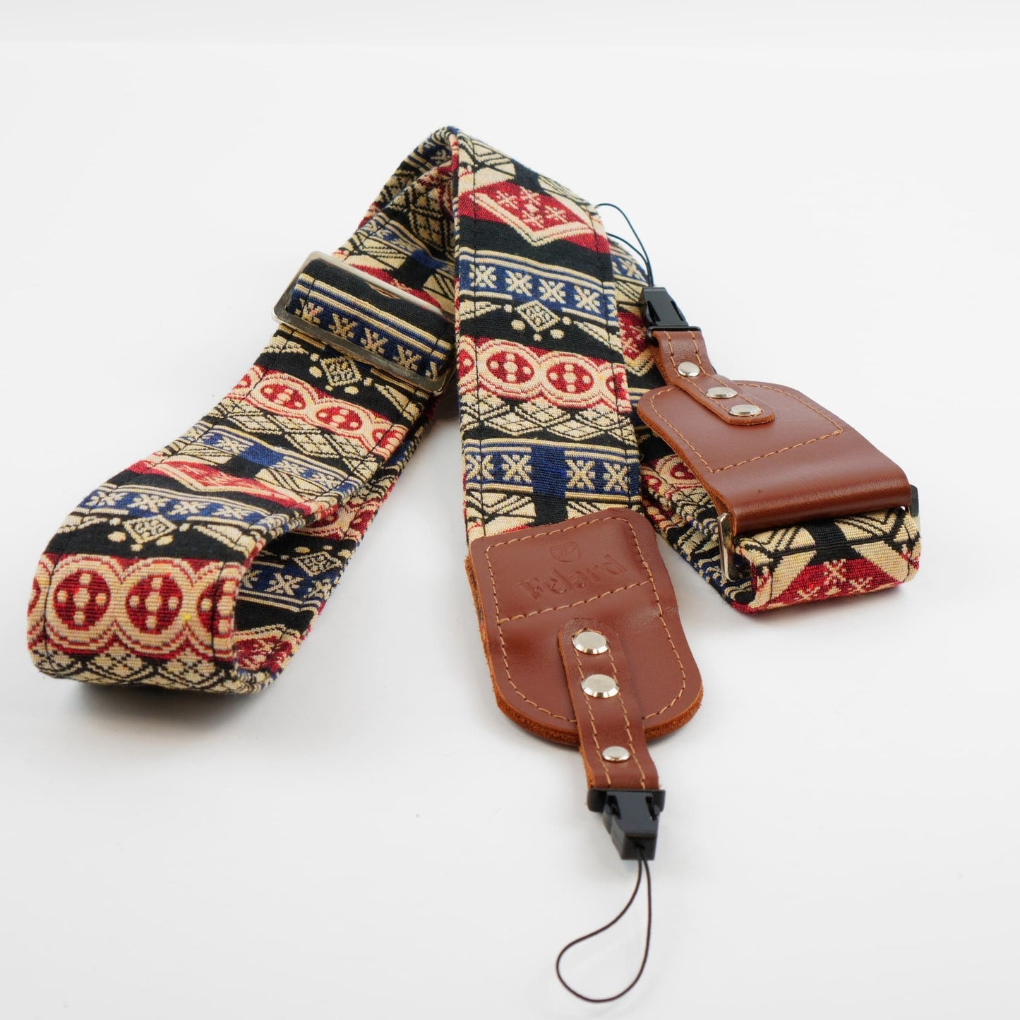 A camera strap featuring a detailed geometric and tribal pattern in beige, navy, red, and black, with brown leather accents and silver-tone metal rivets.
