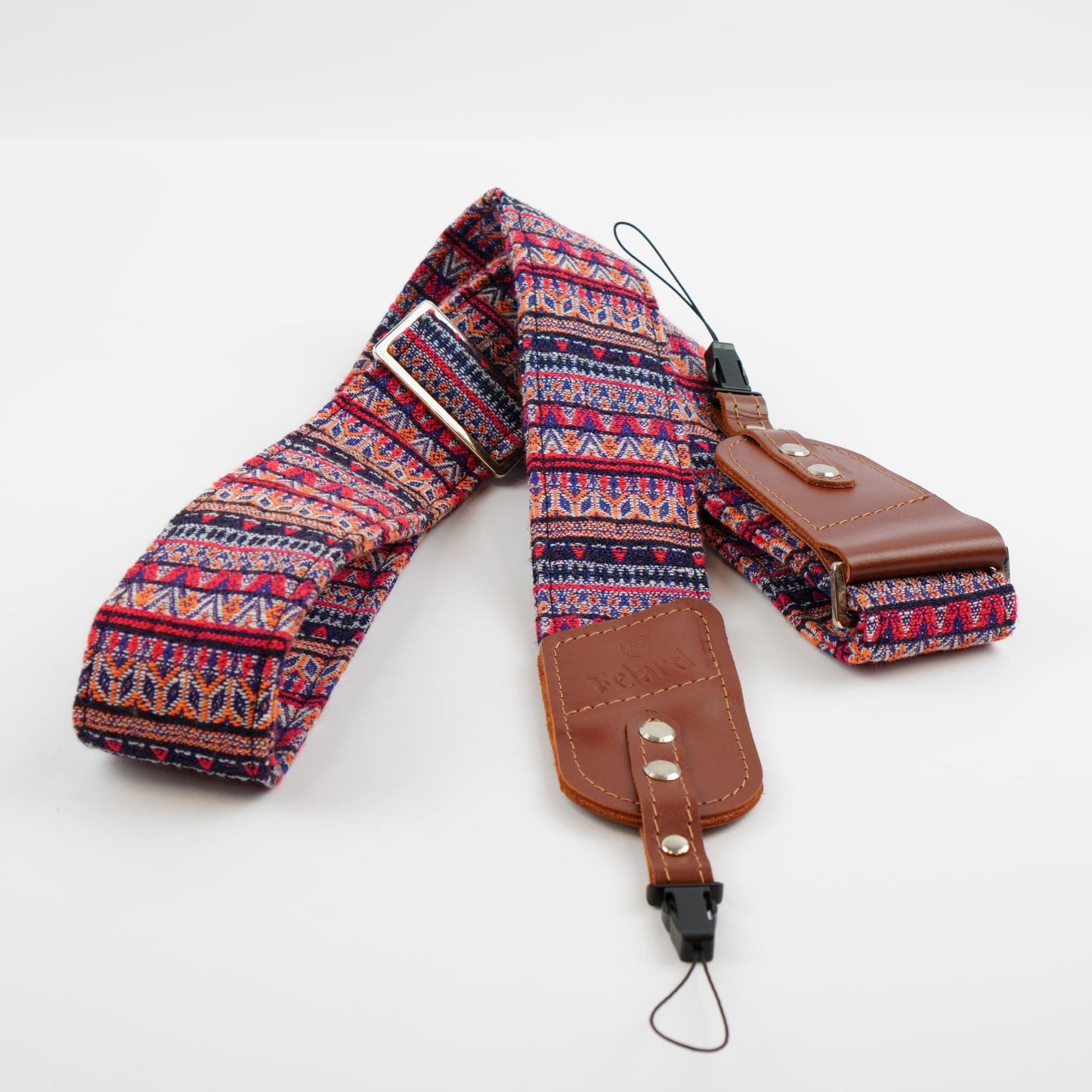 A multicolor patterned camera strap with brown leather accents and metal snap buttons, laid out on a light gray background.
