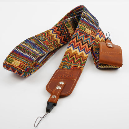 A multicolor woven guitar strap with a brown leather end displayed on a clean white background.