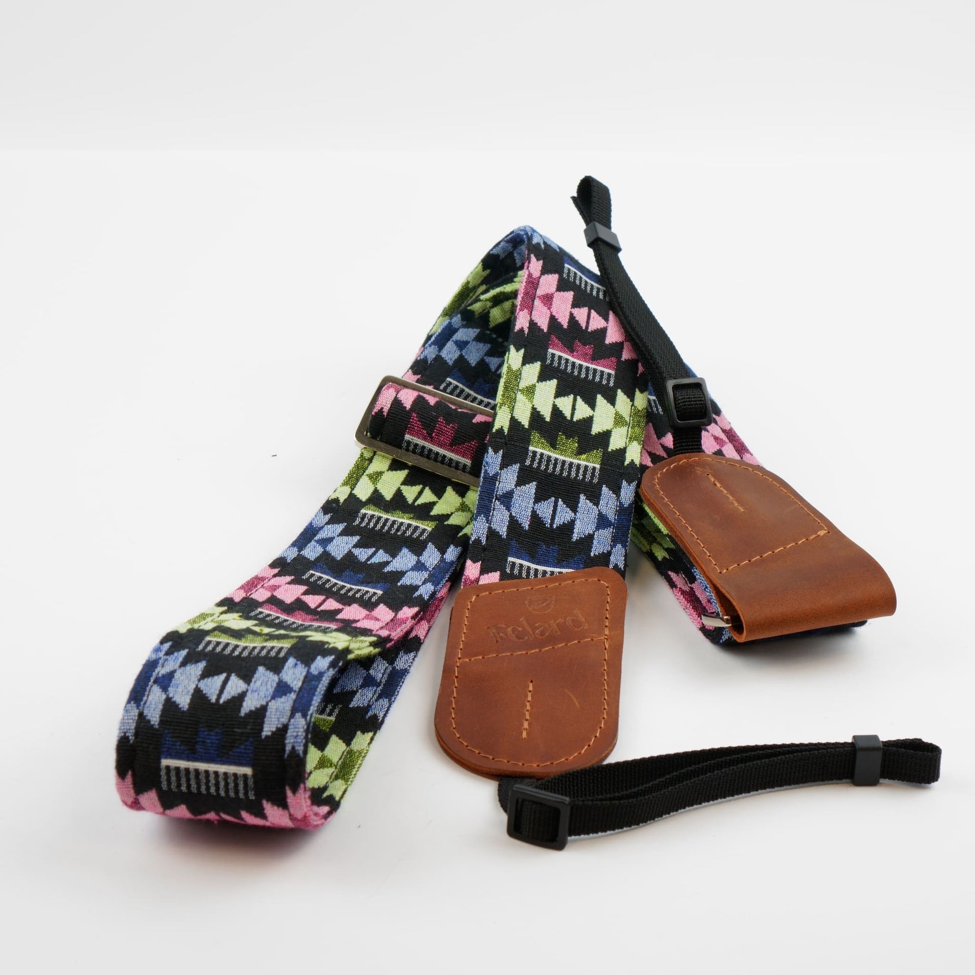 A camera strap with a colorful geometric pattern in pink, green, blue, and black, featuring brown leather end caps and a black adjustable wrist strap, displayed on a clean white background.