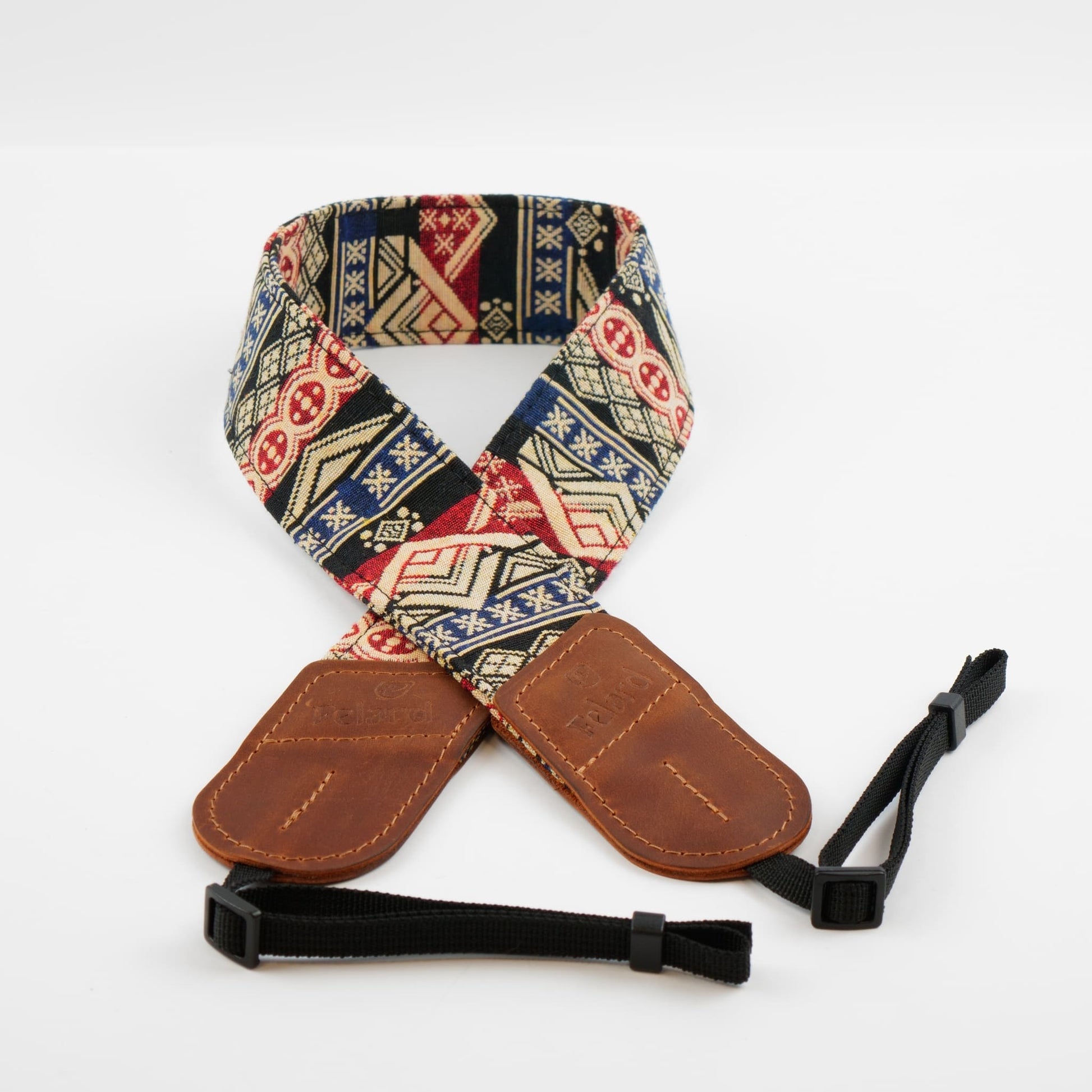 A camera strap featuring a colorful geometric patterned fabric body with brown leather end caps and a black adjustable webbing loop with a plastic buckle, displayed on a clean white background.