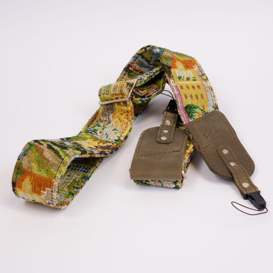 A camera strap featuring a colorful landscape patterned fabric and gray leather accents, displayed on a clean white background.