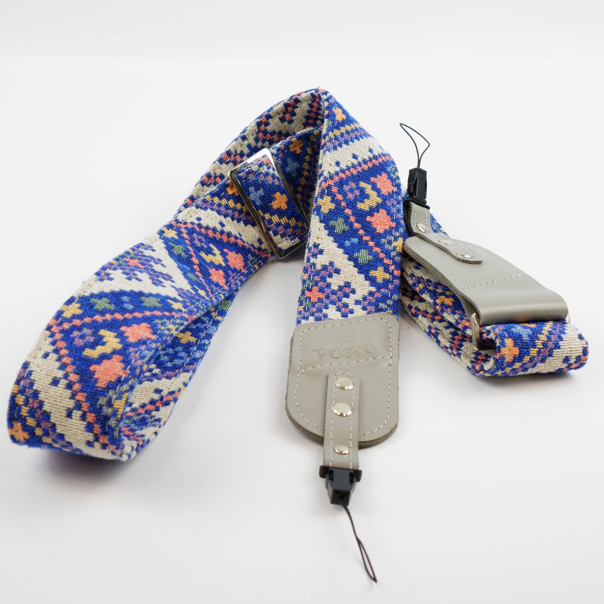 A camera strap with a colorful geometric pattern in blue, pink, and cream, featuring light gray leather-like hardware and a black quick-release buckle.
