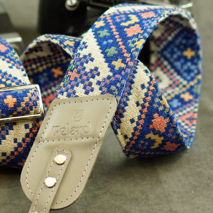 A close-up of a patterned fabric camera strap with a beige leather and the brand name 'Felard' embossed on it, set against a dark gray background.