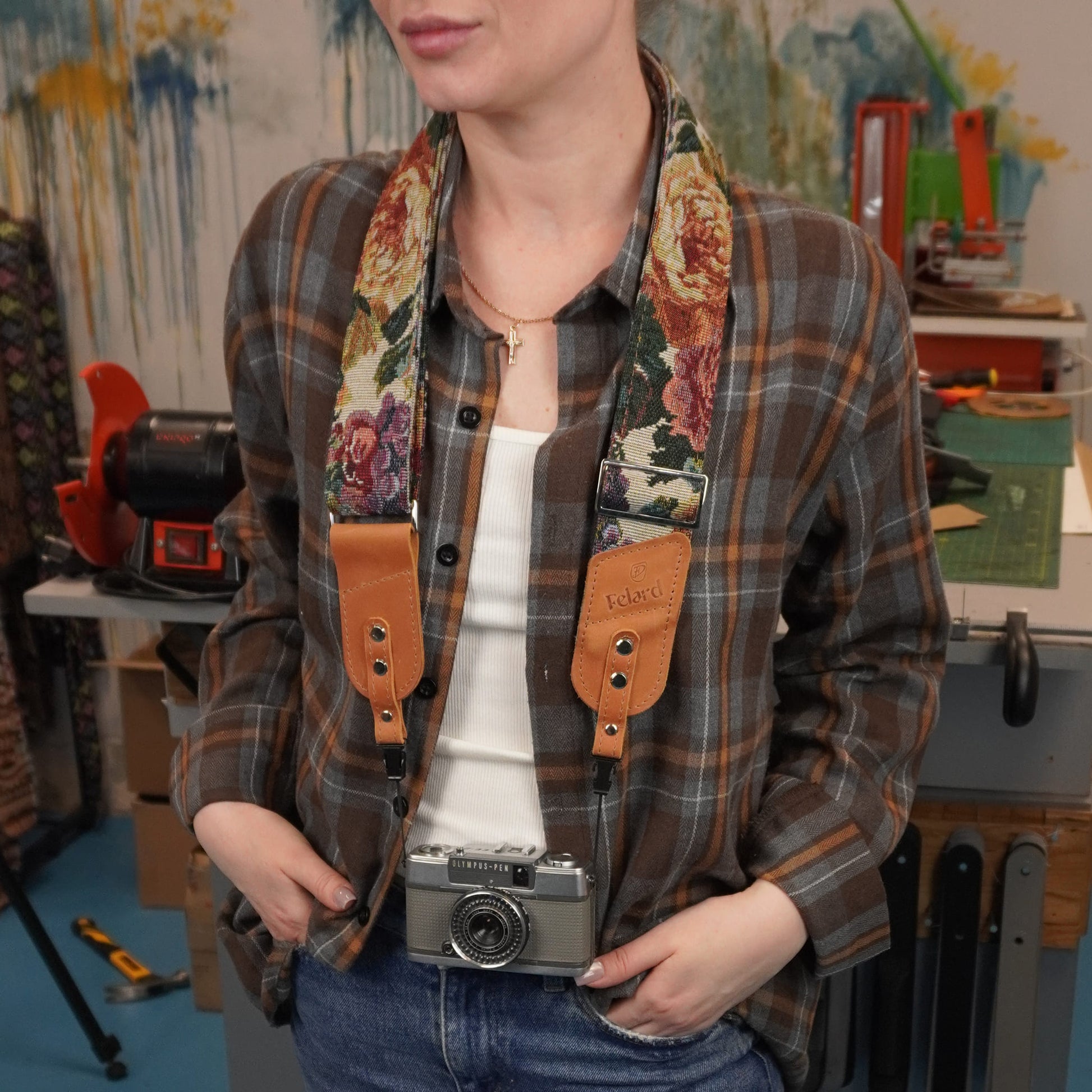 A person with a floral-patterned camera strap featuring tan leather details around the neck and holding a vintage silver camera.