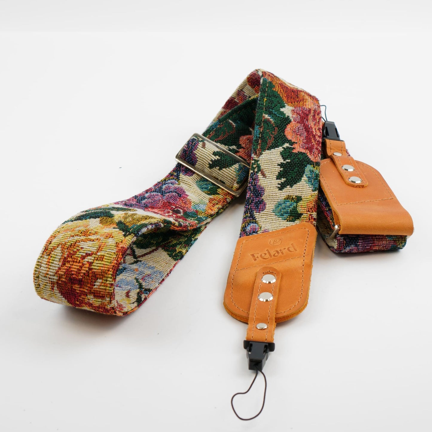 A floral tapestry camera strap with tan leather end pieces and a matching leather pouch, shown on a plain white background. The brand name 'Felard' is embossed on the leather.
