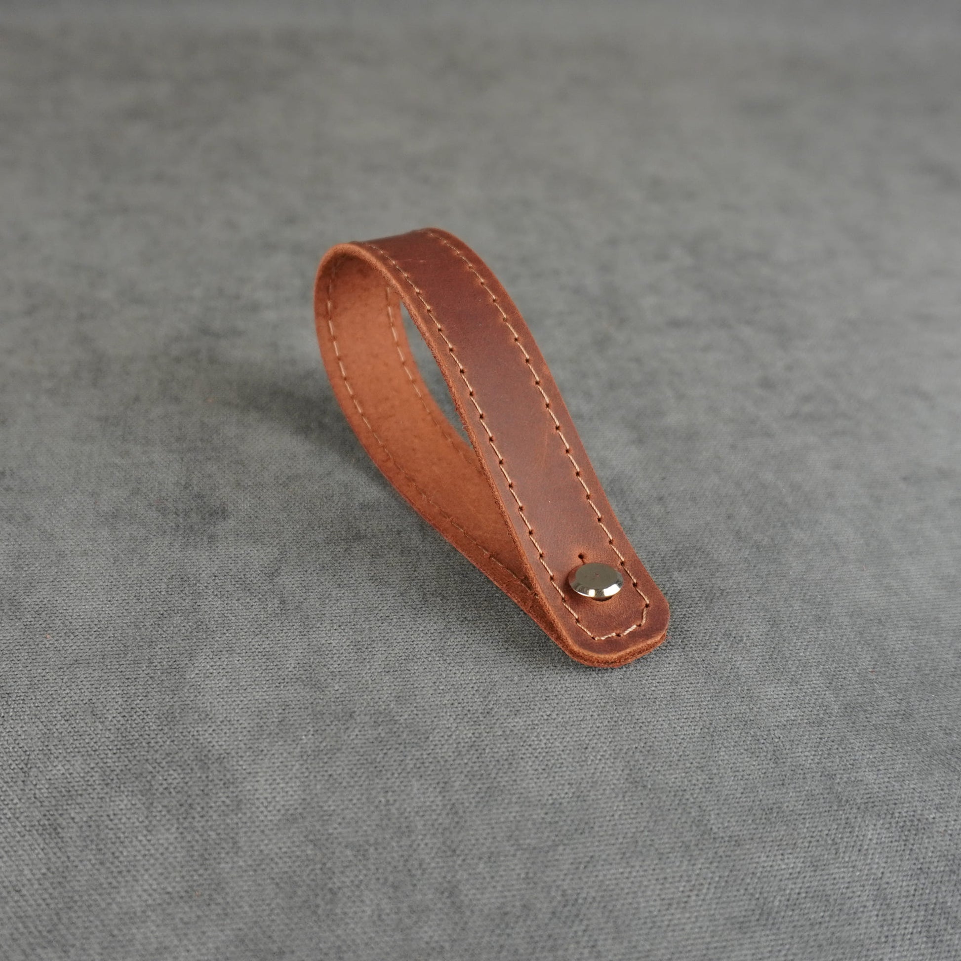  dark cognac matte leather strap headstock adapter with a single silver metal rivet, photographed on a textured gray background.