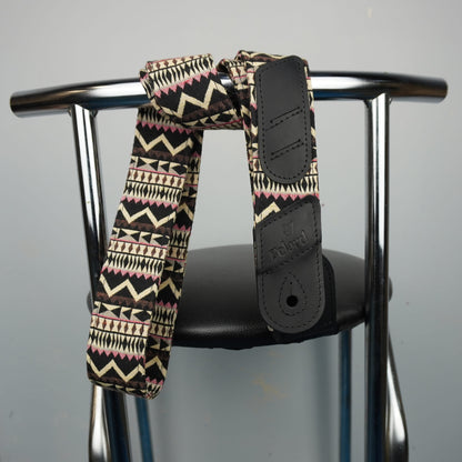 A patterned shoulder strap with black faux-leather end pieces draped over the backrest of a metal chair against a plain light gray wall.