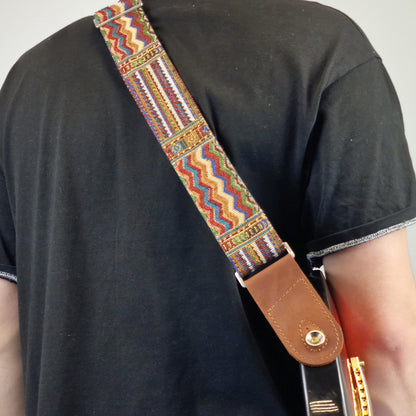 colorful geometric patterned guitar strap with a brown leather end piece.